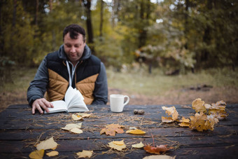 年轻的男人。坐在秋天公园木表格饮料<strong>茶</strong>读取书温暖的黑暗秋天<strong>大气</strong>软焦点模糊复制空间