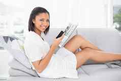 逗乐年轻的黑暗头发的女人白色衣服阅读杂志