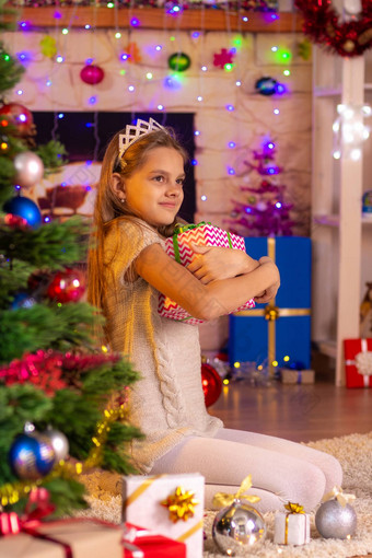 十岁的女孩坐在圣诞节树拥抱礼物