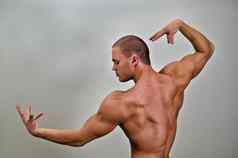 肌肉发达的健美运动员摆姿势灰色背景