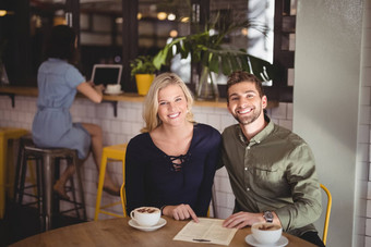 微笑年轻的夫妇坐着<strong>咖啡菜单</strong>表格咖啡馆
