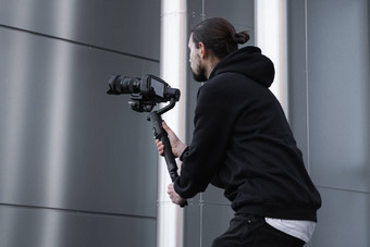年轻的专业电视录像制作人持有专业相机轴健身球稳定剂为设备帮助使高质量<strong>视频</strong>摇晃摄影师穿<strong>白色</strong>连帽衫使<strong>视频</strong>