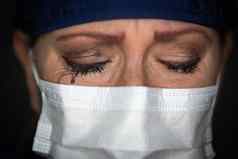泪流满面的强调女医生护士穿医疗脸面具黑暗背景