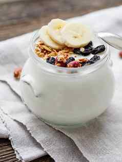 自然自制的酸奶玻璃Jar健康的食物早餐牛奶什锦早餐Jar格兰诺拉麦片香蕉片亚麻桌布木表格