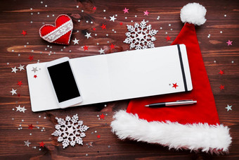 圣诞节一年背景智能手机红色的圣诞老人的他记事本笔圣诞节装饰球星星银闪闪发光的雪花五彩纸屑木表格的地方文本
