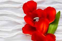 一对婚礼订婚环钻石红色的郁金香自然背景象征爱婚姻关闭