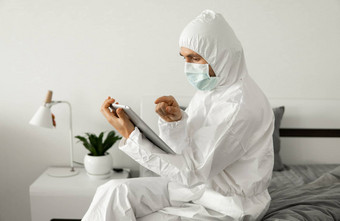 男人。保护白色西装医疗面具工作首页床上平板电脑冠状病毒疫情远程工作流感大流行保持首页科维德检疫概念