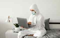 男人。保护白色西装医疗面具工作首页床上移动PC冠状病毒疫情远程工作流感大流行保持首页科维德检疫概念
