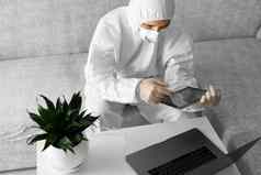 男人。保护白色西装医疗面具工作首页沙发移动PC平板电脑冠状病毒疫情远程工作流感大流行保持首页科维德检疫概念