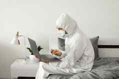 男人。保护白色西装医疗面具工作首页床上移动PC冠状病毒疫情远程工作流感大流行保持首页科维德检疫概念