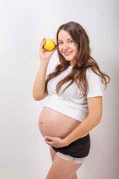 图像怀孕了女人触碰大肚子持有黄色的苹果手白色背景