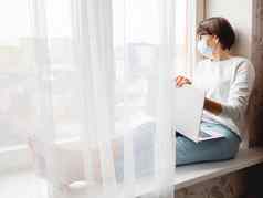 女人医疗面具远程作品首页坐在窗口窗台上移动PC膝盖封锁检疫冠状病毒科维德隔离首页