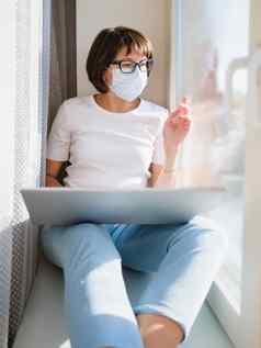 女人医疗面具远程作品首页坐在窗口窗台上移动PC膝盖封锁检疫冠状病毒科维德隔离首页