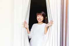 宽微笑美丽的亚洲女人打开窗帘窗口年轻的快乐女人纺织折叠布料