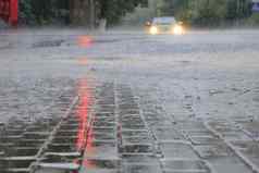 重雨人行道上沥青路照亮红色的交通光