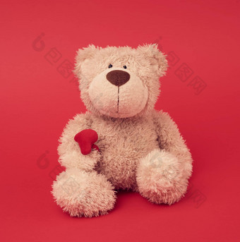 棕色（的）泰迪熊玩具坐着红色的背景