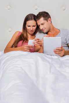 肖像年轻的有吸引力的女人显示智能手机的男朋友玩游戏数字平板电脑床上