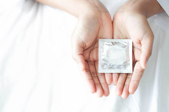 关闭女人手持有避孕套说谎白色床上健康