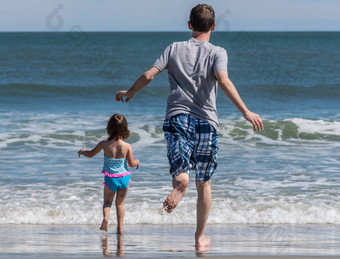 后视图父亲年轻的女儿运行海洋波