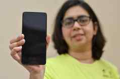 年轻的女人显示空白移动电话黑色的屏幕黄色的背景复制空间应用程序概念快乐智能手机用户空白屏幕广告