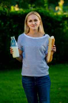 肖像年轻的女人站花园持有玻璃瓶牛奶魔杖