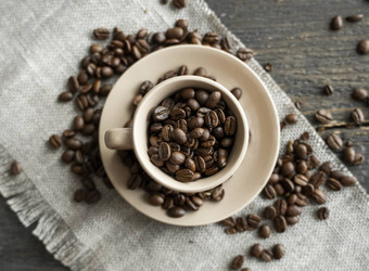 咖啡杯填满新鲜的Arabica罗布斯塔咖啡豆子分散咖啡豆子亚麻纺织木表格