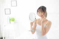 美丽的脸年轻的亚洲女人快乐微笑镜子化妆美面部女孩护肤品化妆品治疗刷新女清洁迷人的健康的概念