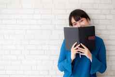 美丽的肖像年轻的亚洲女人快乐隐藏覆盖书水泥砖混凝土背景女孩站开放笔记本阅读学习教育知识概念