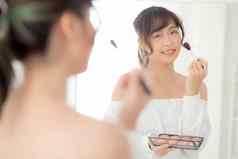 美肖像年轻的亚洲女人微笑脸镜子应用化妆刷脸颊卧室美丽的女孩持有脸红的人皮肤护理化妆品表格时尚概念