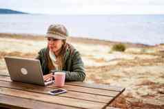 互联网女自由工作户外海度假胜地坐着木表格穿秋冬衣服羊毛他茶杯关闭铝移动PC改变生活使在线工作
