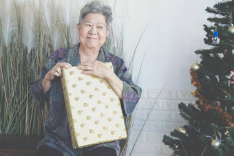 亚洲老女人上了年纪的高级女持有礼物现在盒子圣诞节树