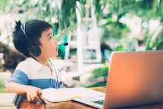 亚洲男孩穿耳机集中学习移动PC电脑家庭作业孩子们研究电子学习笔记本正常的活动爱好孩子教育概念
