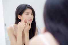 美丽的年轻的亚洲女人镜子触摸脸痤疮坐在治疗美女孩问题美皮肤皱纹面部房间首页化妆化妆品概念