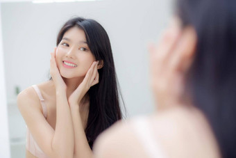 美丽的年轻的亚洲女人微笑镜子检查脸皮肤护理化妆品复兴卫生美女孩快乐清洁面部奶油乳液健康