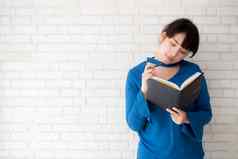 美丽的亚洲女人微笑站思考写作笔记本混凝土水泥白色背景首页女孩家庭作业书教育生活方式概念