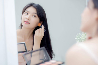 美年轻的亚洲女人快乐微笑脸镜子应用化妆刷子脸颊房间美丽的女孩持有刷化妆面部皮肤护理化妆品概念