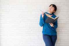 美丽的亚洲女人微笑站思考写作笔记本混凝土水泥白色背景首页女孩家庭作业书教育生活方式概念