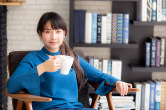美丽的年轻的亚洲女人坐着椅子安慰放松生活房间首页喝杯咖啡茶饮料生活方式亚洲女孩休闲健康的健康满意