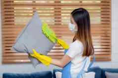 年轻的亚洲女人脸面具手套清洁灰尘除尘器沙发垫子首页女孩做家务卫生房子管家服务健康护理生活方式概念