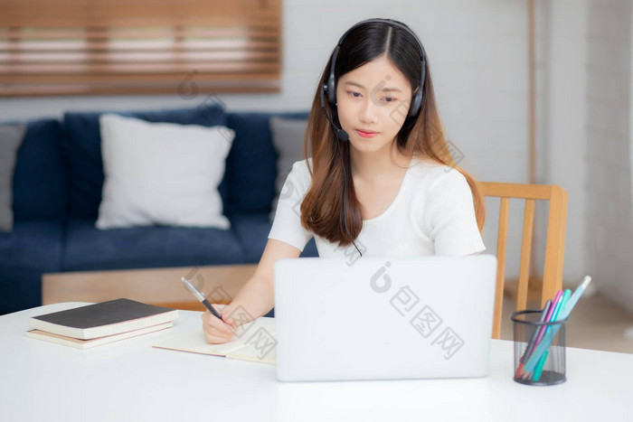 年轻的亚洲女人穿耳机研究在线电子学习桌子上女孩穿耳机学习互联网移动PC电脑首页正常的距离教育培训