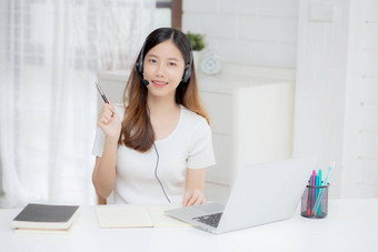 年轻的亚洲女人穿耳机研究在线电子学习桌子上女孩穿耳机学习互联网移动PC电脑首页正常的距离教育培训