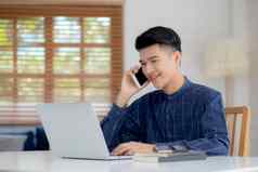 年轻的亚洲男人。会说话的电话工作首页移动PC电脑自由笔记本互联网在线说话智能手机国内生活业务沟通概念