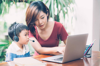 年轻的亚洲妈妈。儿子移动PC电脑研究<strong>学习</strong>首页男孩穿耳机电子<strong>学习</strong>距离老师妈妈支持孩子教育概念