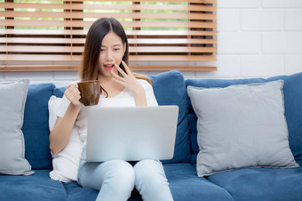 年轻的亚洲业务女人微笑工作首页移动PC电脑在线沙发生活房间自由女孩笔记本喝咖啡沙发上正常的生活方式概念