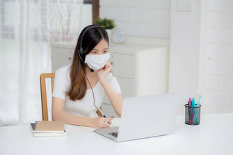 年轻的亚洲女人穿耳机研究在线电子学习桌子上女孩穿耳机学习互联网移动PC电脑首页正常的距离<strong>教育培训</strong>