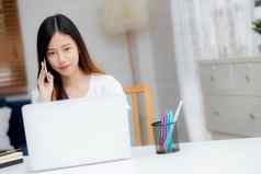 年轻的亚洲女人会说话的电话工作首页移动PC电脑自由笔记本互联网在线说话智能手机国内生活业务沟通概念