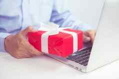 手男人。持有红色的礼物盒子移动PC电脑木表格在线购物给现在圣诞节一天周年纪念日季节庆祝社会距离