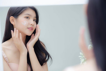美丽的年轻的亚洲女人微笑镜子检查脸皮肤护理化妆品复兴卫生美女孩快乐清洁面部奶油乳液健康