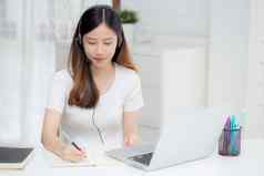 年轻的亚洲女人穿耳机研究在线电子学习桌子上女孩穿耳机学习互联网移动PC电脑首页正常的距离教育培训