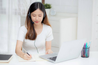 年轻的亚洲女人穿<strong>耳机</strong>研究在线电子学习桌子上女孩穿<strong>耳机</strong>学习互联网移动PC电脑<strong>首页</strong>正常的距离教育培训